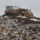 A bulldozer pushes a large pile of trash on top of a landfill hill.